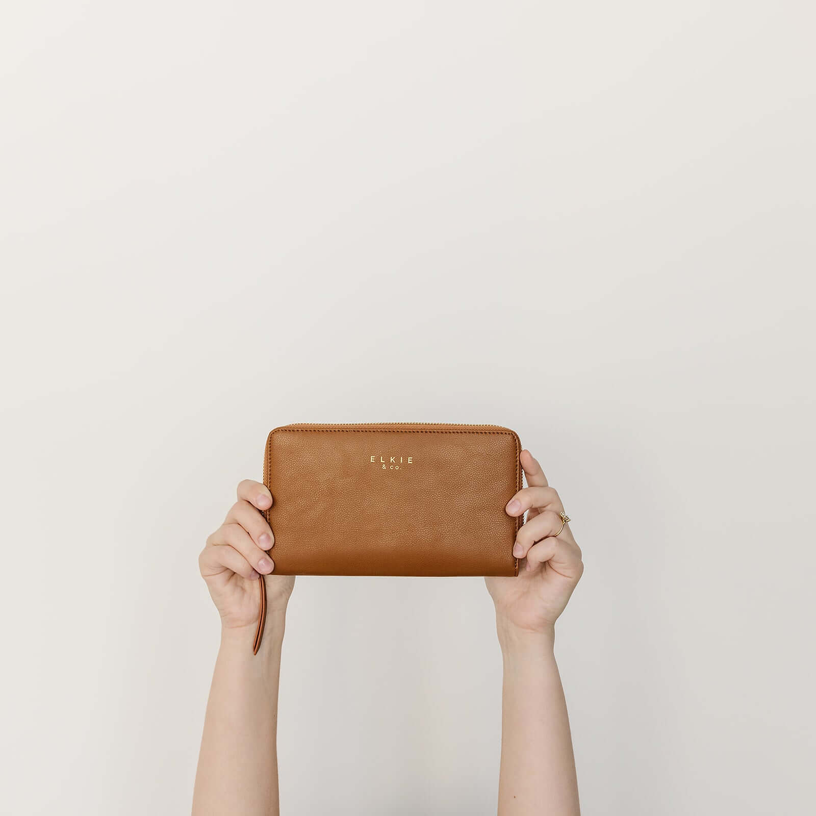 Hands holding Elkie & Co. Vegan Leather Wallet against a white background.