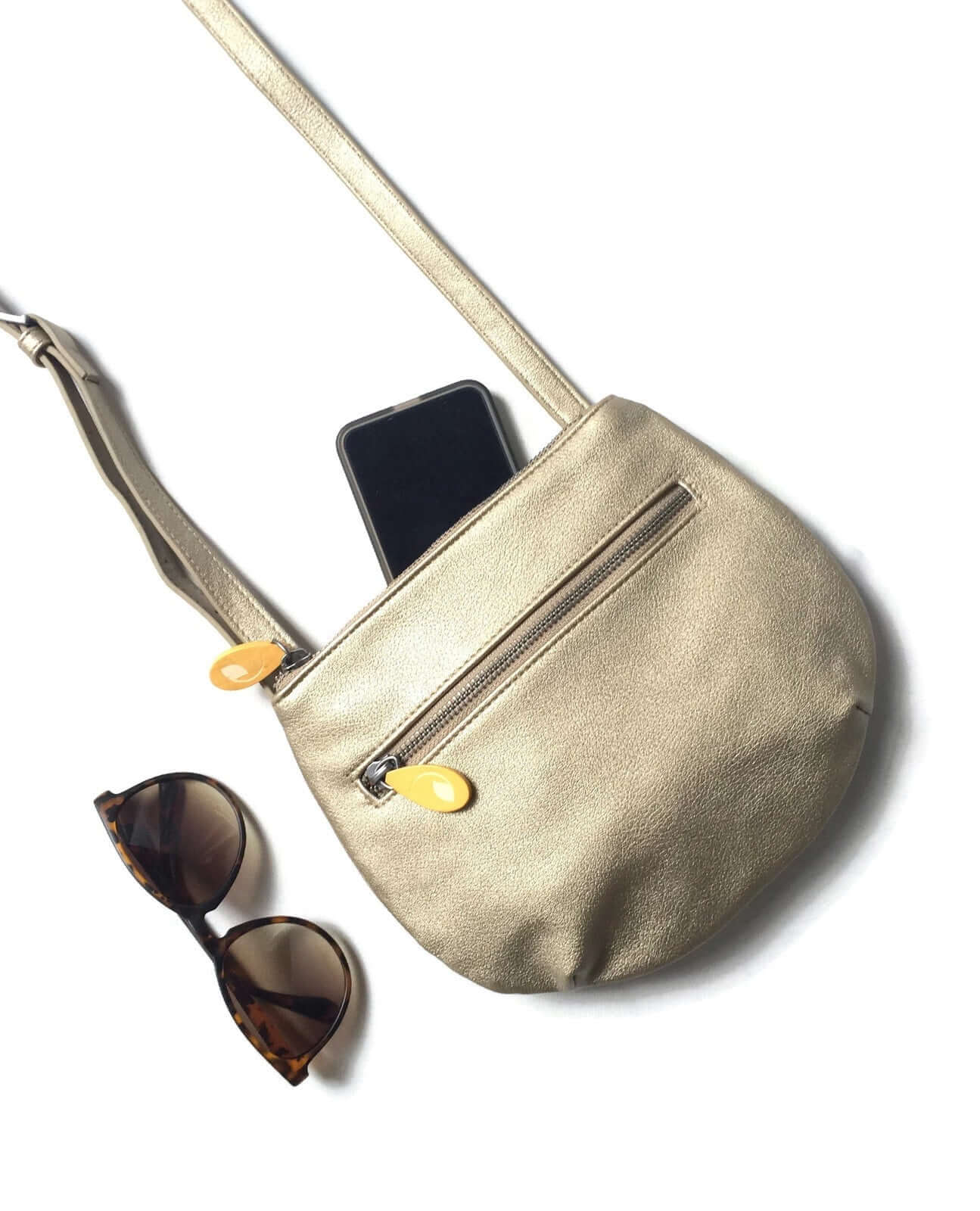 Vegan leather gold crossbody bag with adjustable strap and phone in zippered compartment, alongside sunglasses, perfect for everyday essentials.