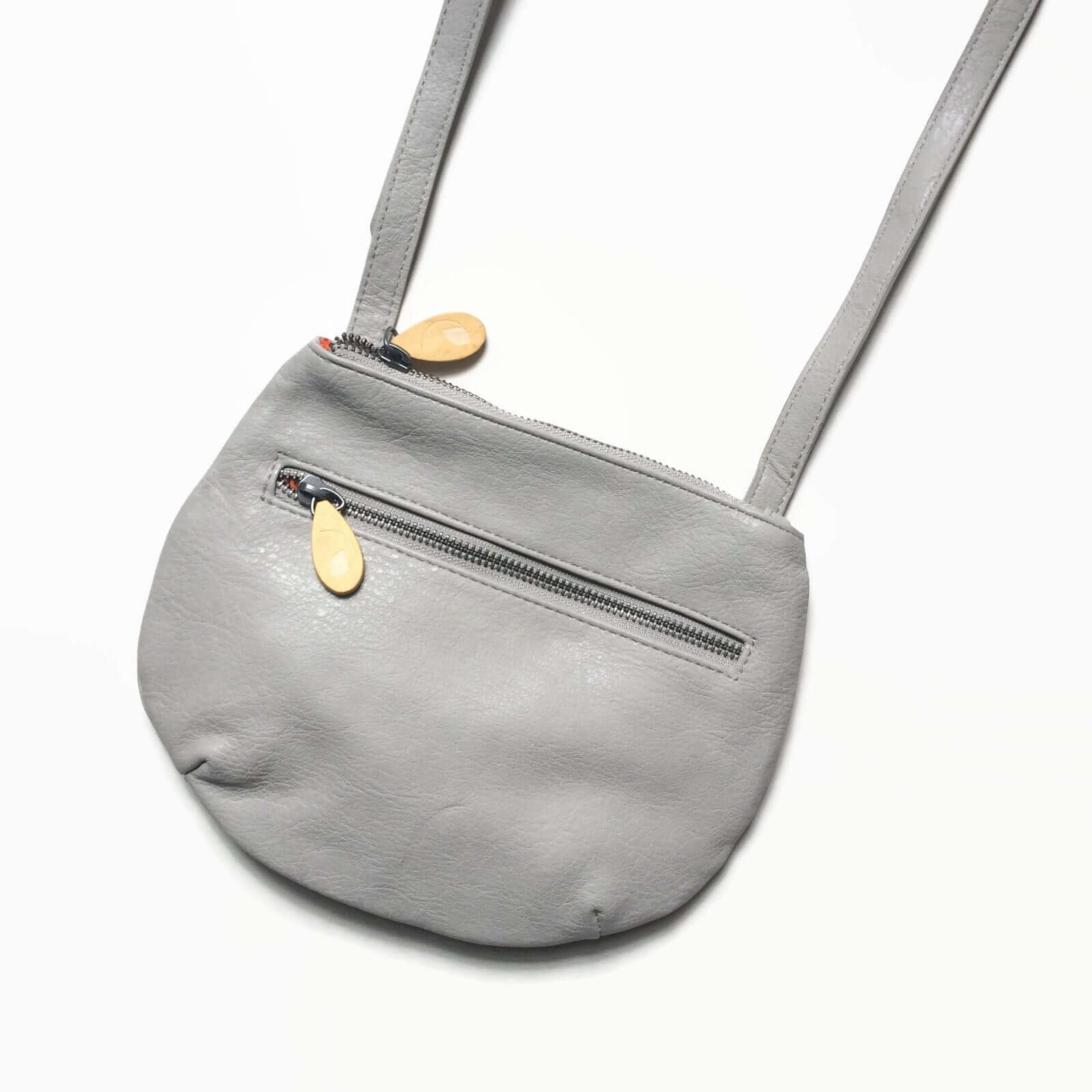 Grey Willoughby Crossbody Bag in vegan leather with two zippered compartments and wood zip pullers, adjustable 24" strap, and bright orange lining.