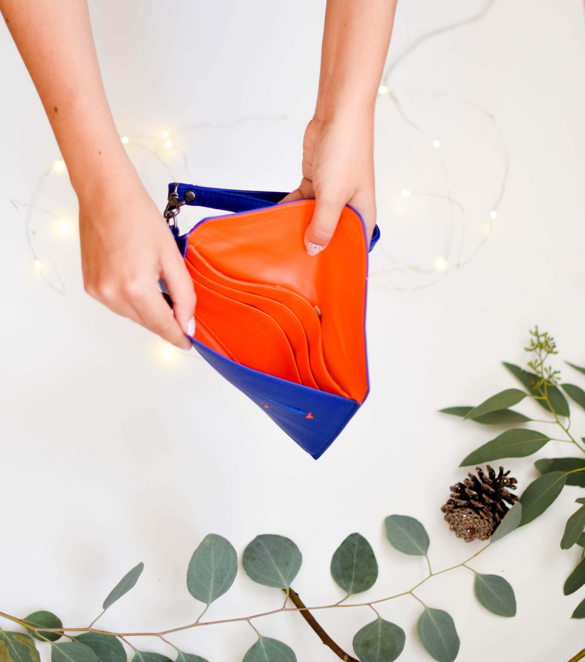 Person opening Delancey Wristlet Wallet made of vegan leather showing vibrant orange interior with card slots.