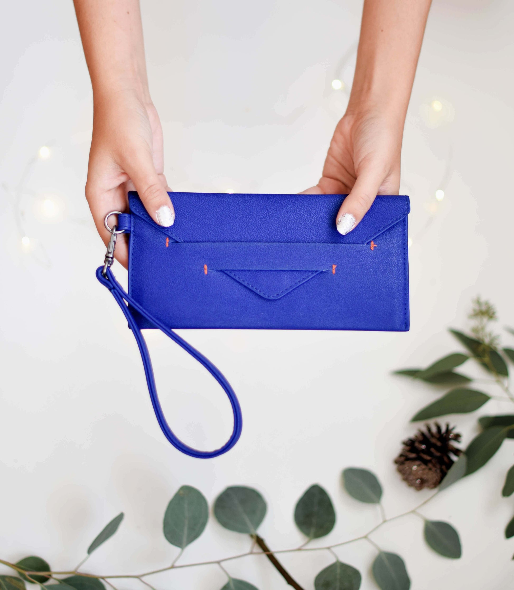 Hands holding Delancey Wristlet Wallet in blue vegan leather with detachable wrist strap and hidden magnet closure