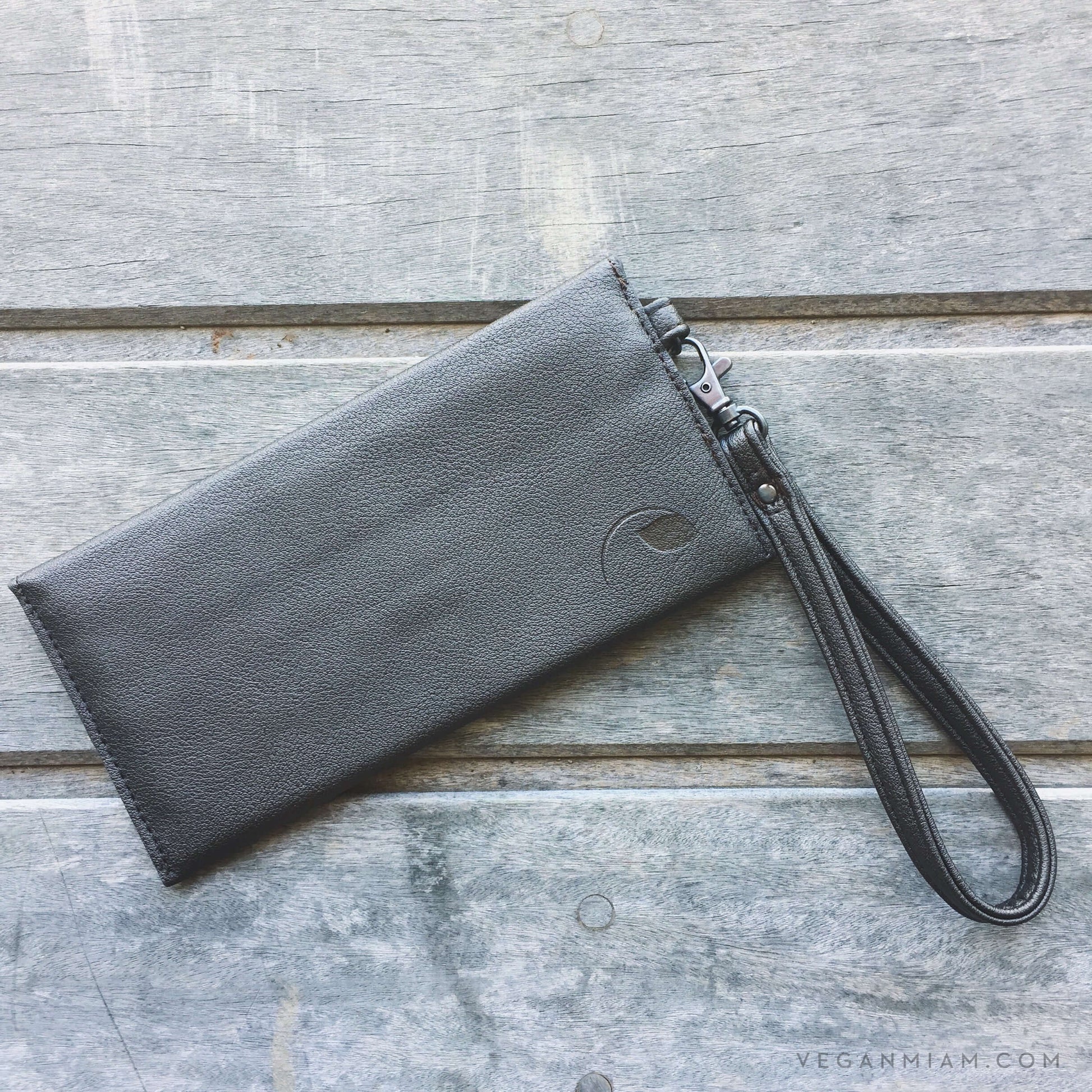 Delancey Wristlet Wallet made from grey vegan leather with detachable wrist strap on wooden background.