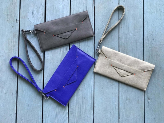 Delancey Vegan Wallet collection in various colors with wrist straps on a wooden surface