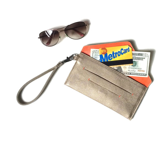 Delancey Vegan Wallet in beige with wrist strap, holding MetroCard and cash, next to stylish sunglasses.