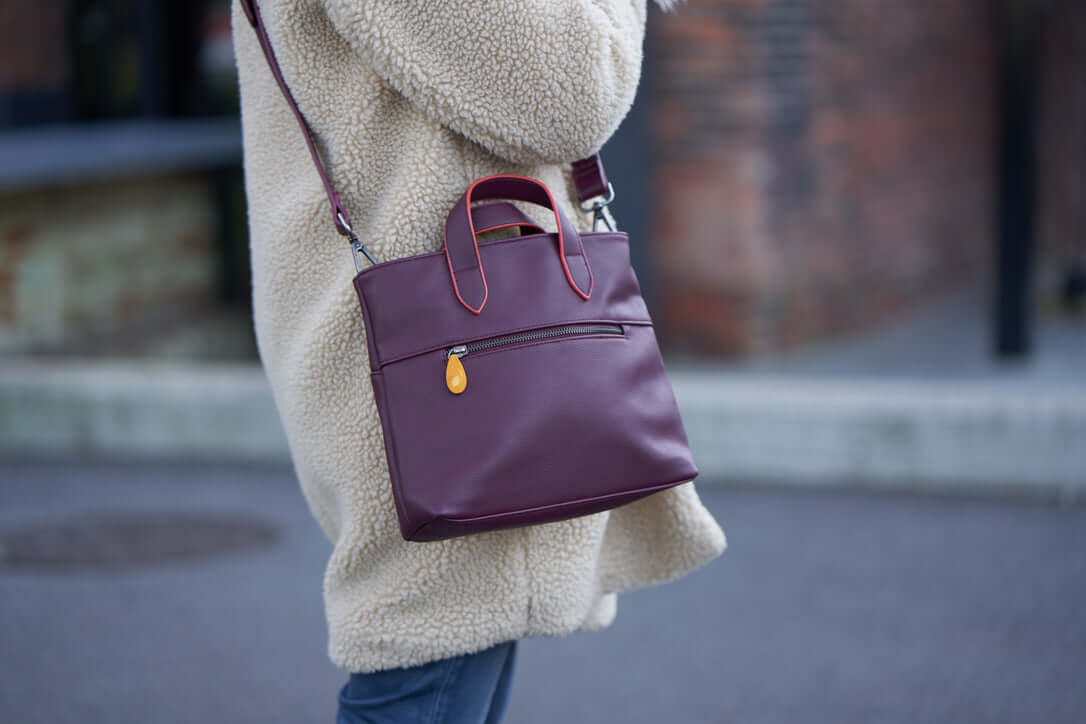 Person wearing the Atlantic Crossbody Satchel in maroon with wood zip puller and orange-edged handles.