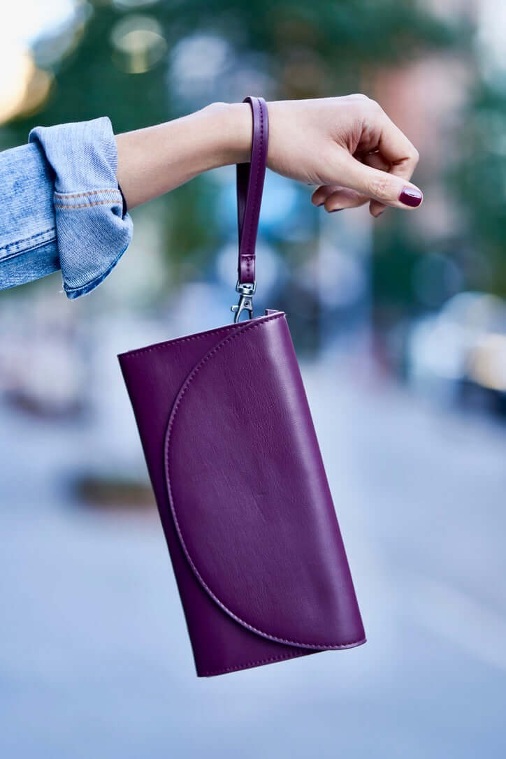 Purple Clark Phone Wallet by Canopy Verde in vegan leather with detachable wrist strap, held by a hand in denim sleeve