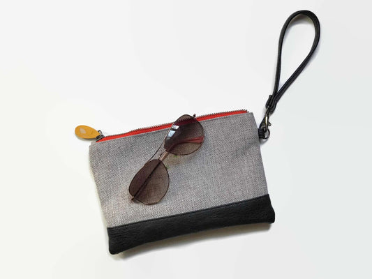 Gowanus Wristlet Clutch with black strap, gray body, and red zipper, featuring a pair of sunglasses on top