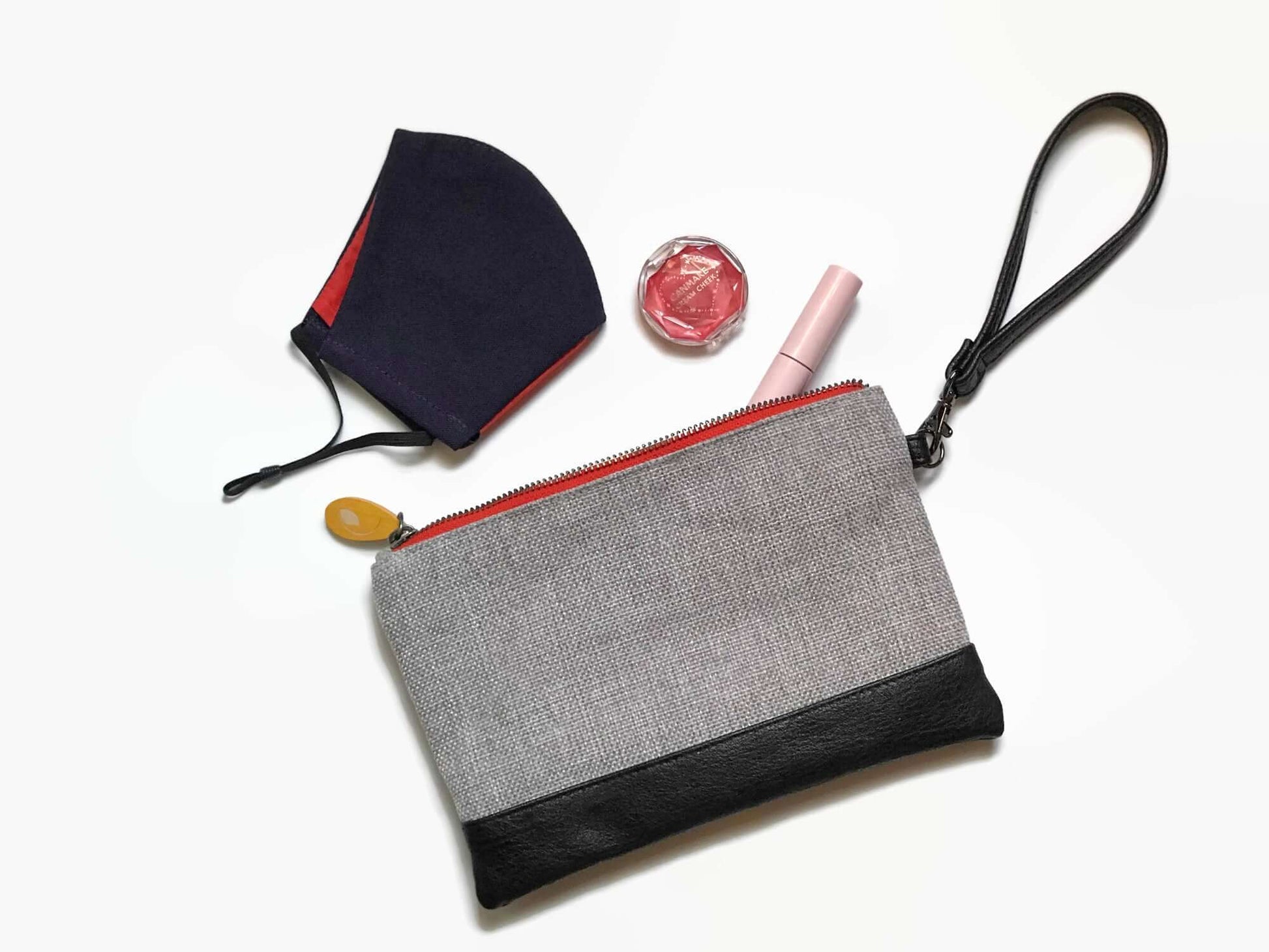 Gowanus Wristlet Clutch in gray and black with a mask, lip balm, and blush on a white background