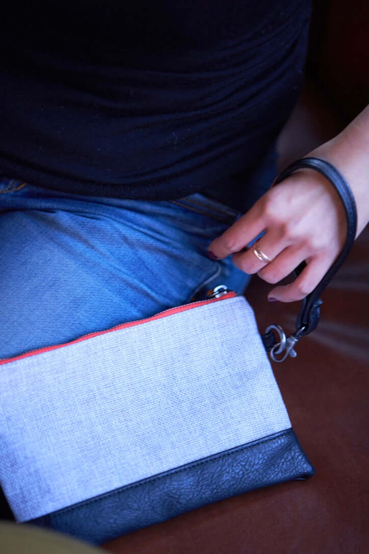 Person holding Gowanus Wristlet Clutch in gray and black vegan leather with wrist strap, showcasing its chic and versatile design.