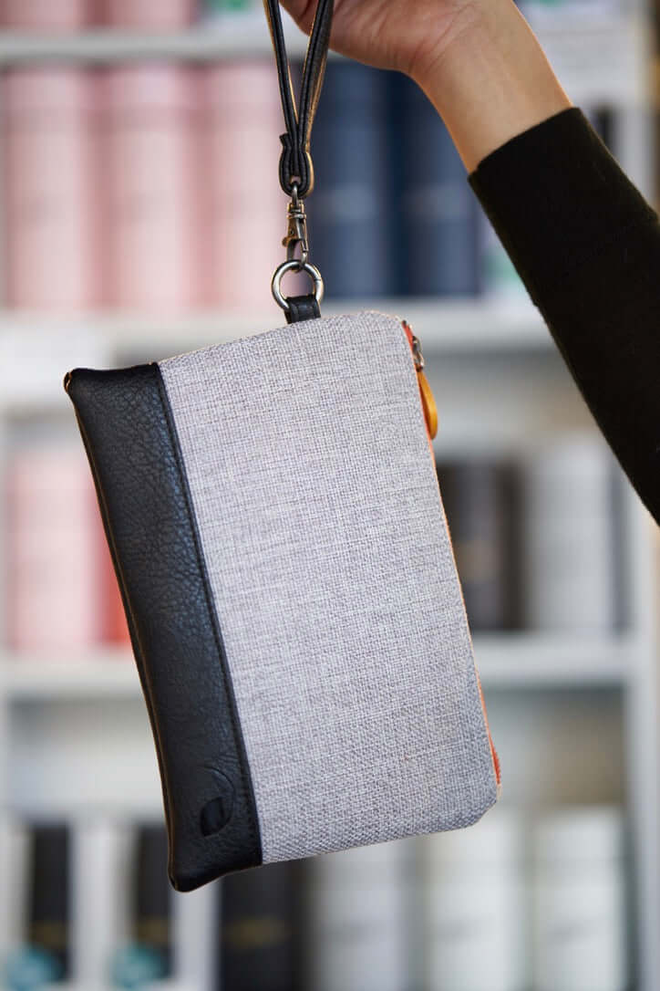 Hand holding the Gowanus Wristlet Clutch with black vegan leather, gray polyester, and wood trims, featuring a wrist strap