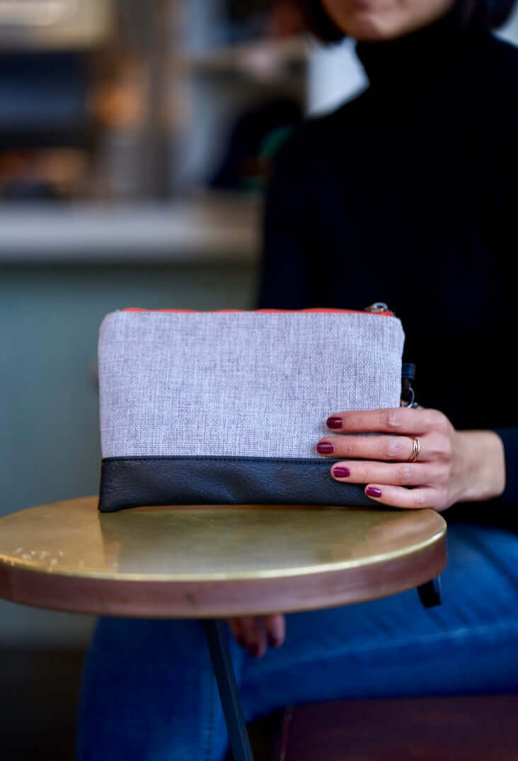 Woman holding the versatile Gowanus Wristlet Clutch made of polyester and vegan leather with wood trims, featuring zippered pockets.