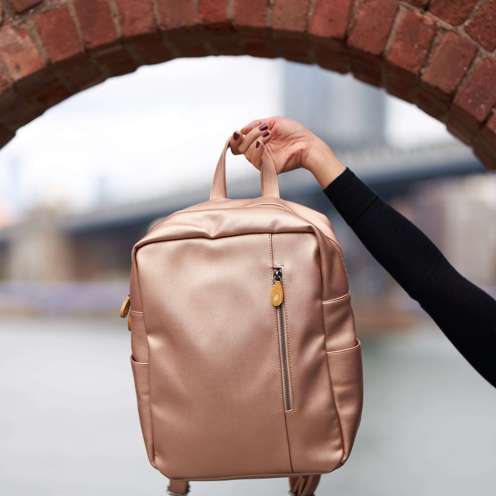 Lenox Vegan Leather Backpack with handle held up against a brick arch background.