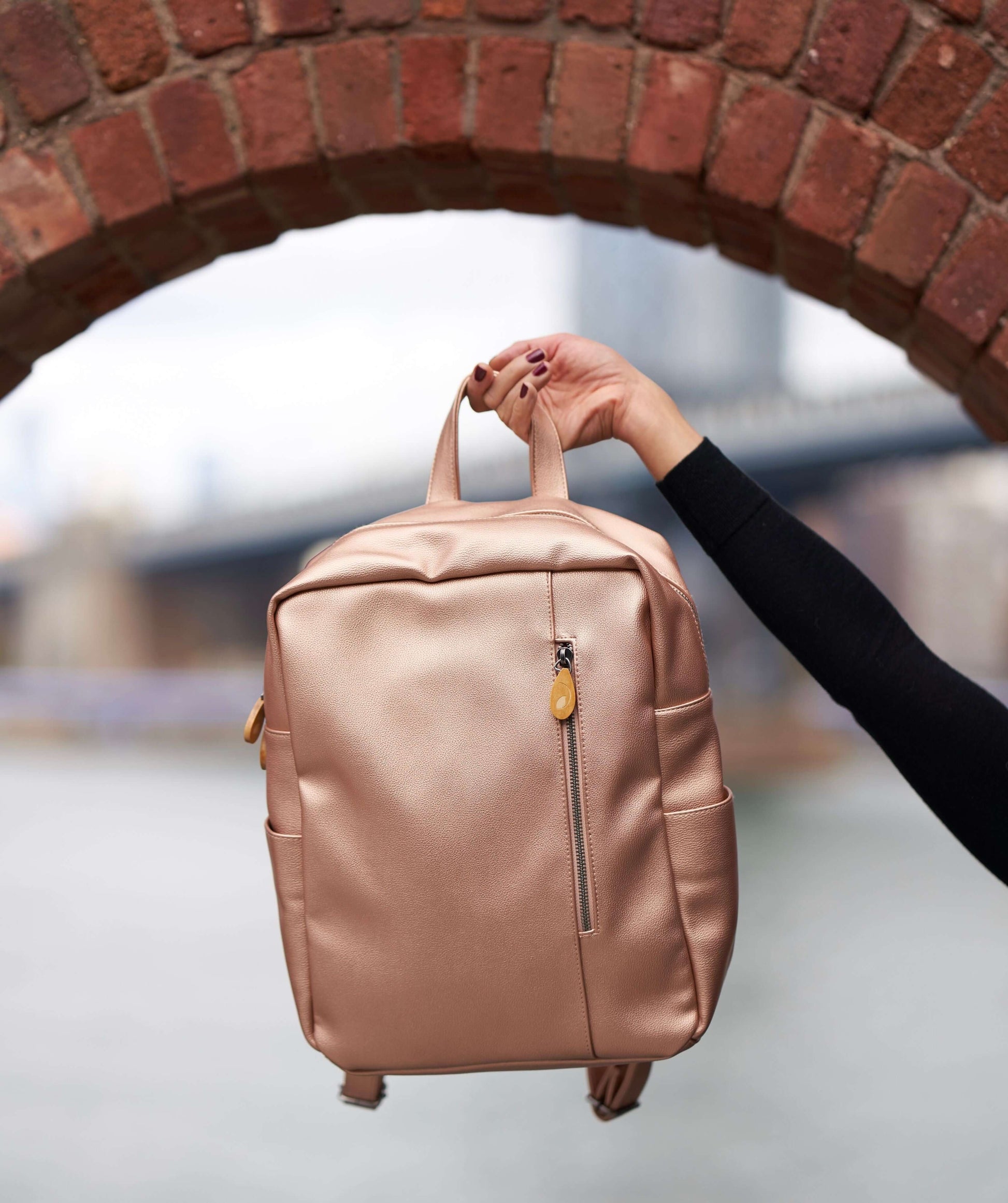 Lenox Vegan Leather Backpack with handle held up against a brick arch background.