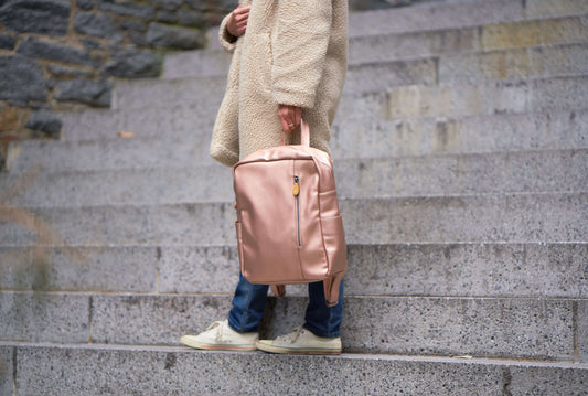 Person holding Lenox vegan leather backpack on stone steps, showcasing sleek and minimalist design