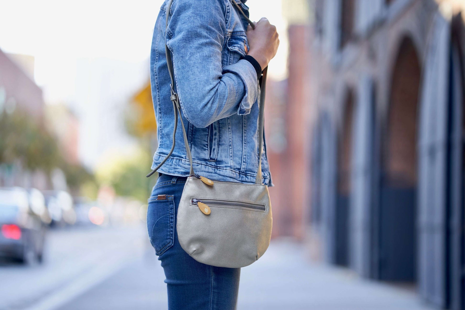 Woman wearing Willoughby Crossbody Bag in vegan leather, featuring two zippered compartments, adjustable strap, and wood zip pullers